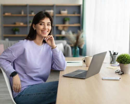 portrait-of-smiling-young-woman-sitting-at-desk.jpg